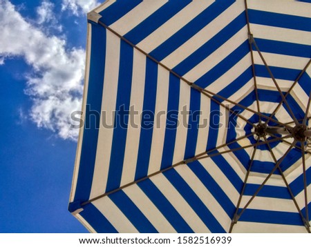 A relaxing wallpaper with striped blue and white textured parasol and cloudy blue sky in the background