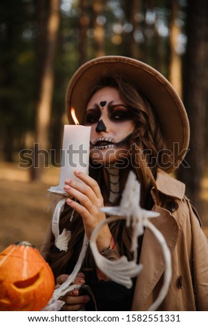 woman in zombie costume in a dark forest for halloween with a candle and fire