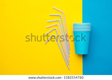 Blue paper cups with drinking colored plastic straws yellow and blue background. Set for party. Top view. Minimalist Style. Copy, empty space for text