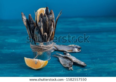 Small, salted fish. Near the slices of lemon. Good snack for beer. Sea fish. Background tinted in classic modern blue 2020. 