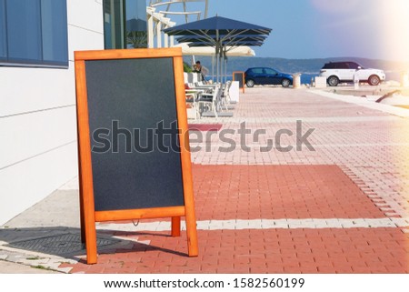 Black board menu black color for text, message or advertising. Mockup is standing near the restaurant in sea coast. Sunny day.