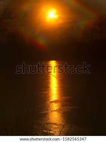 Beauty of evening sunset over a frozen lake.
 Sun is reflected across the entire width of the reservoir and forms a brilliant path.