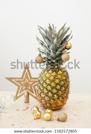 Pineapple decorated wih Christmas golden balls on white background, holiday Christmas or new year concept of decor. Exotic summer festive picture. Zero waste.