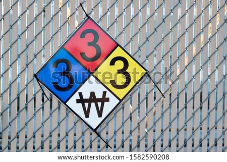 Hazardous Materials Classification Sign attached to a wire fence. The colors represent fire, health and reactivity hazards, the numbers are severity. Bottom W icon means use no water.