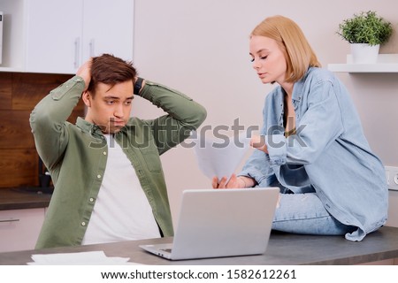 couple using modern laptop computer, looking worried and sad, studying online, solving financial problems at home, anxious, searching for job, reading bad news, searching, talking using papers
