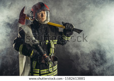 young caucasian fireman holding hammer, risking his life to save people from fire, wearing protective uniform