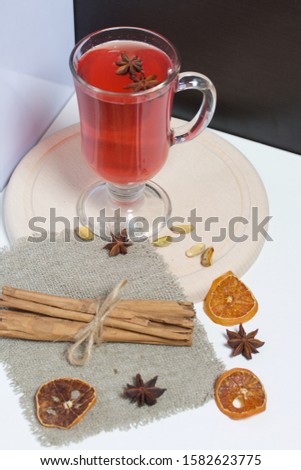 Red drink in a glass goblet. Anise stars float in it. Nearby on linen are pistachios, dried mandarin rings and cinnamon sticks.