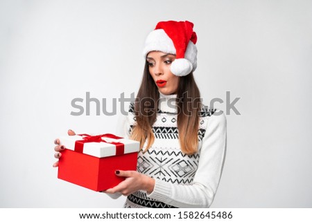 Close up portrait beautifiul caucasian woman in red Santa hat on white studio background. Christmas New Year holiday concept Surprised Cute girl teeth smiling positive emotions with red gift box