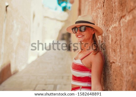 Young positive woman in hat on Mediterranean street toothy smile