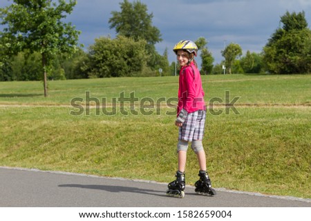 Smiling girl enjoying rolller skating in a park with a turned head backwards and looking into camera