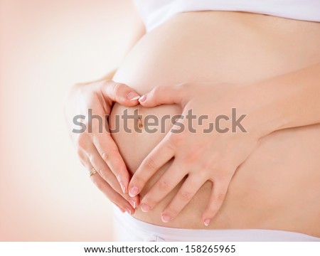 Pregnant Woman holding her hands in a heart shape on her baby bump. Pregnant Belly with fingers Heart symbol. Maternity concept. Baby Shower  Royalty-Free Stock Photo #158265965