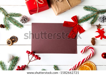 Beautiful Christmas composition on wooden white background. Empty card with Christmas present boxes, snowy fir branches, conifer cones, caramel stick, gift. New Year. Top view, copy space.
