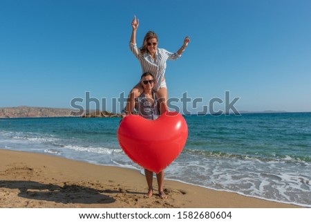 Young couple having fun on the beach with a big heart balloon. Summer love concept.
