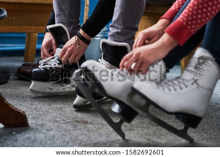 Young couple preparing to a skating. Close-up photo of their hands tying shoelaces of ice hockey skates