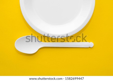 Plastic white spoon and plate on yellow background. Cooking utensil. Top view. Minimalist Style. Copy, empty space for text