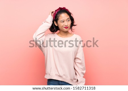 Asian young woman over isolated pink background having doubts while scratching head