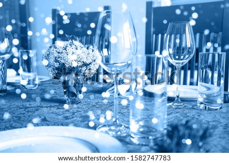 Holiday party blurred background made from decorated table with bouquet of flowers and colorful lights bokeh. Selective focus. Christmas dinner. Classic Blue color 2020 concept.