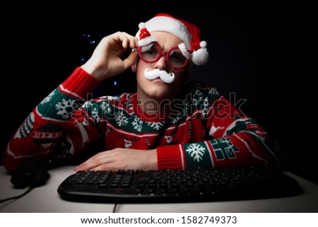young guy plays on a computer in the New Year at night, a lonely student gamer at Christmas sits near a computer