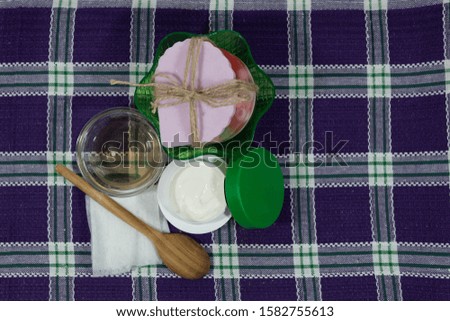 On a checkered napkin, cream for the skin, in a saucer olive oil, a wooden spoon, wet wipes and two pieces of handmade soap.