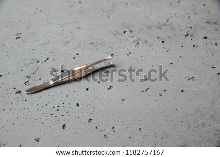 Tweezer on a dark stone background. The concept of taking care of appearance. Use of body care tools.