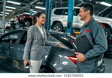 Beautiful businesswoman and auto service mechanic are discussing the work. Car repair and maintenance.