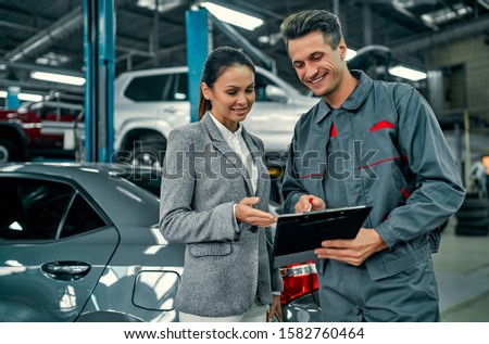 Beautiful businesswoman and auto service mechanic are discussing the work and signing documents. Car repair and maintenance.