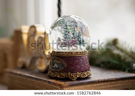 Nostalgic snow globe with horse and sleigh sitting on top of an antique book, among Christmas decorations.