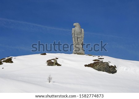 Eagle stone sculpture  on the hill at Simplonpass Switzerland with snow in the ground and blue sky.