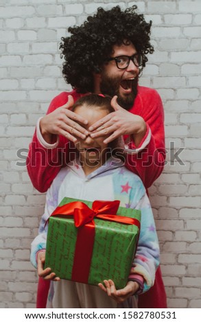 Merry Christmas or happy birthday! Cheerful bearded young man with curly hair in pink dragon pajamas with little daughter in unicorn suit with Christmas gift box. Crazy emotions. Pajamas party