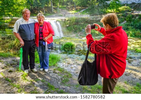 Mature tourists walk and take pictures in the Park at the waterfall on a Sunny day