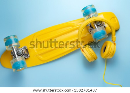Yellow headphones and skateboard or pennyboard on blue background. Music concept.