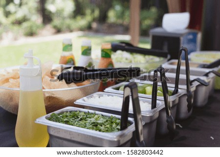 Condiments for a taco bar, including cilantro, onions, lime, with sides of chips and salad