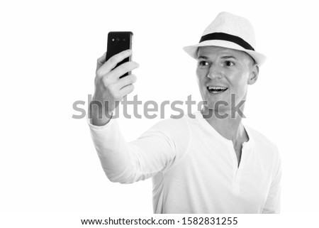 Studio shot of young happy man smiling while taking selfie picture with mobile phone