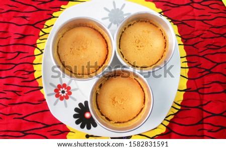 Three Metal Cups of Beans Cake or Nigerian Moi Moi served on a white plate placed on a colorful red and yellow African pattern tablecloth