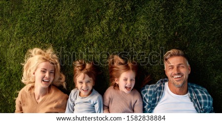 Top view of smiling parents, little girl and boy having fun while lying on a grass. Children, family and nature concept. Horizontal shot