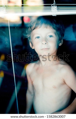 Little cute boy throught window making funny faces, home alone lifestyle concept