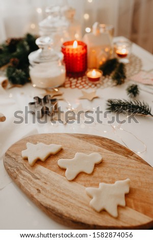 raw cookie in the form of a Christmas tree, snowflakes and a man on a wooden board on the background of Christmas decor, burning candles and garlands