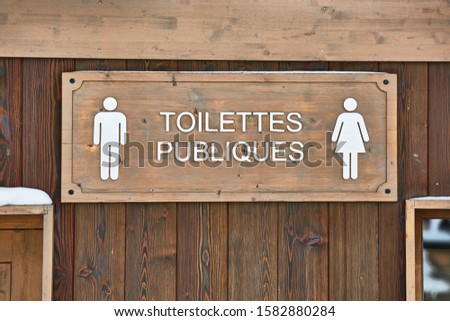 Public toilets signs on a wooden building in France. Sign in French reads Public Toilets translated to English