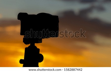 Silhouette of camera on tripod capturing sunset.