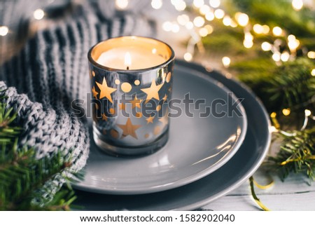 Christmas and New year background with tree branches, burning candle and grey scarf framed by glowing bokeh Selective focus.