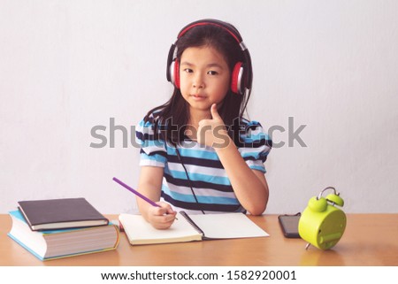 Asian little girl writeing a book and headphones listening to music.
