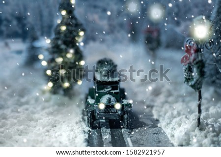 Miniature classic car carrying a christmas tree on snowy road on winter magic background