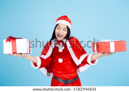 Happy Asian woman in Santa Claus costume holding Christmas  gift box on blue background.