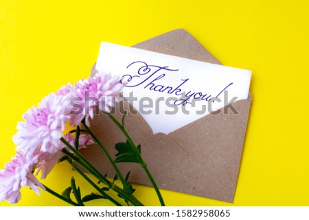 Love envelope and letter with written words thank you with pink chrysanthemum flowers on bright yellow bacground. 