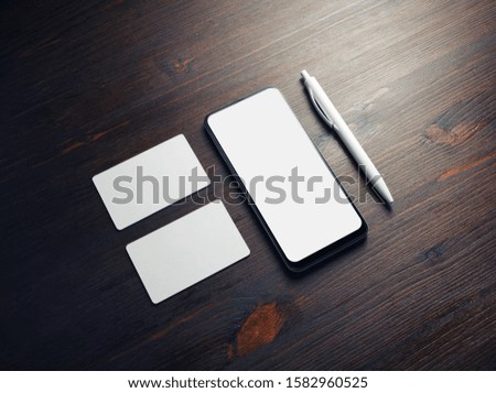 Photo of smartphone with blank screen, business cards and pen on wood table background. Mock-up for branding ID.