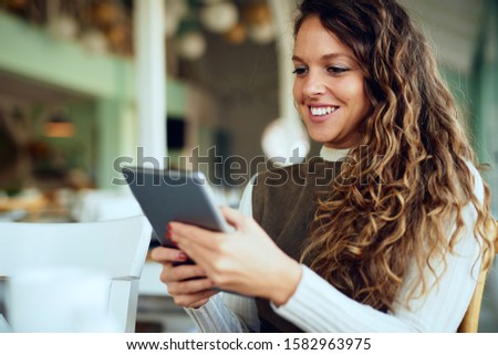 Attractive young curly brunette looking at her tablet and smiling