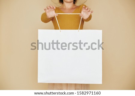 Cropped image of woman showing big white shopping bag without any inscriptions