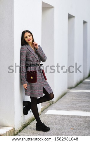 Young beautiful girl with very long hair looking at camera wearing winter coat and cap outdoors. Lifestyle and fashion concept.
