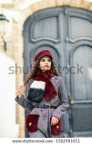 Young beautiful girl with very long hair looking away wearing winter coat and cap outdoors. Lifestyle and fashion concept.