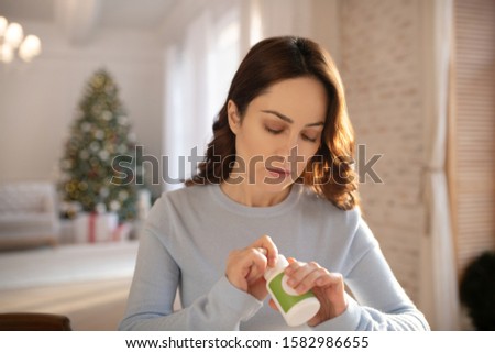 Tome to take pills. Young cute woman in grey homewesar opening a box with vitamins